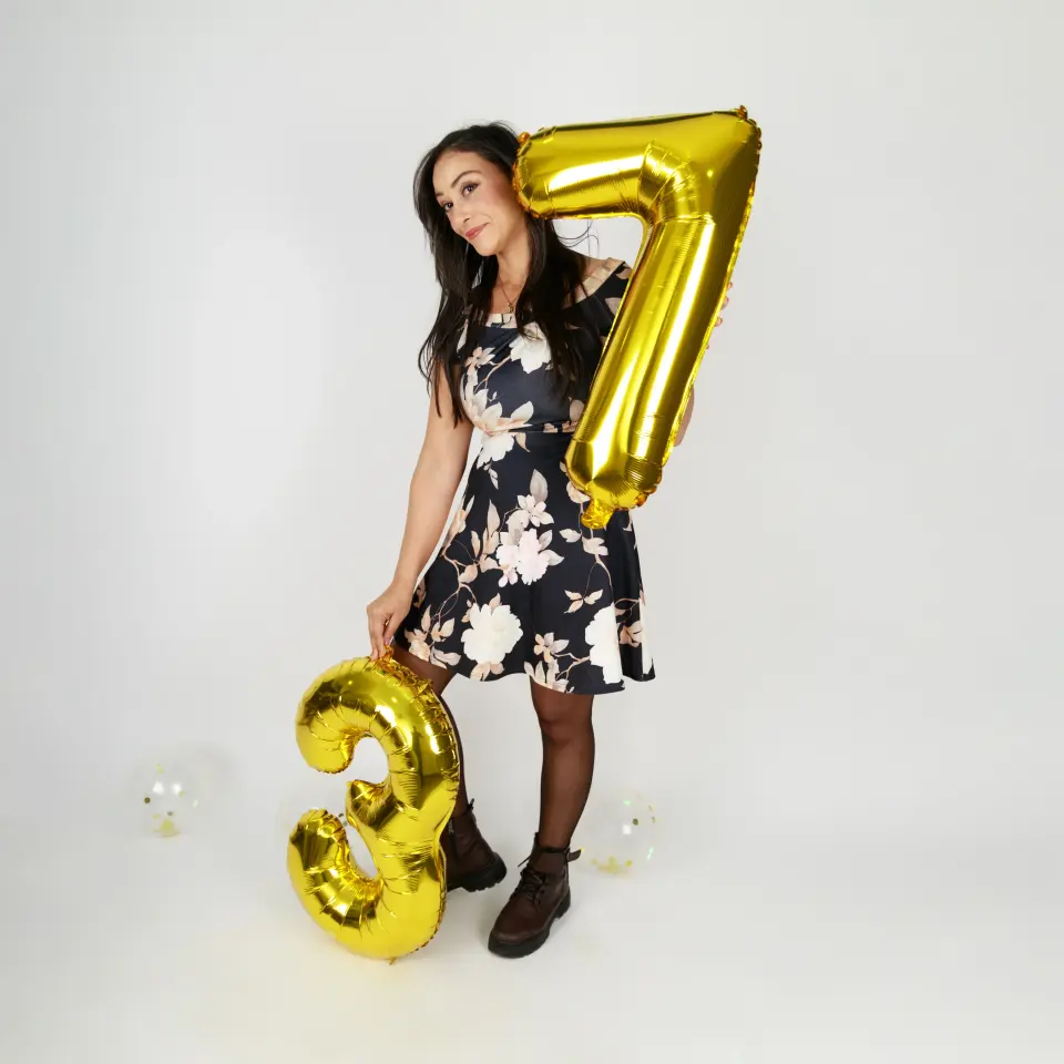 Femme en robe fleurie posant avec des ballons dorés « 37 » en studio