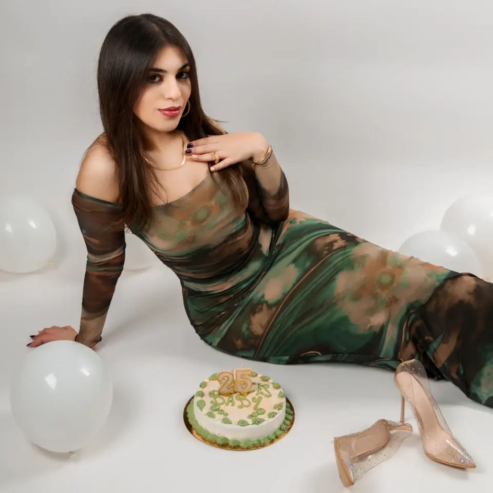 Femme en robe verte allongée en studio entre des ballons blancs et un gâteau