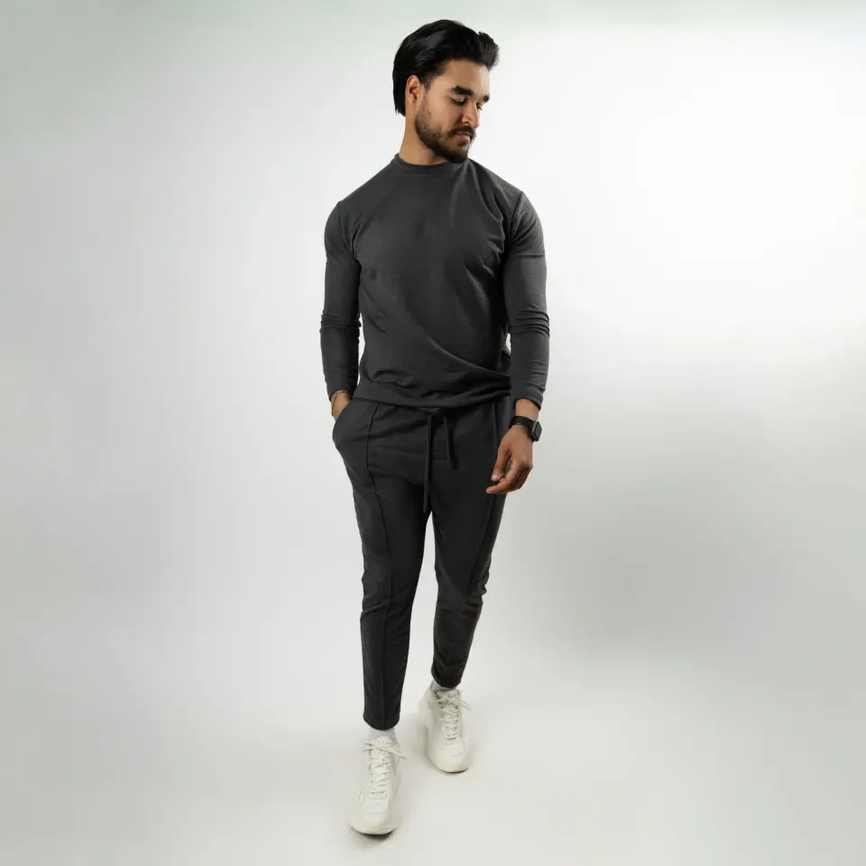Homme en tenue grise posant les mains dans les poches sur fond blanc