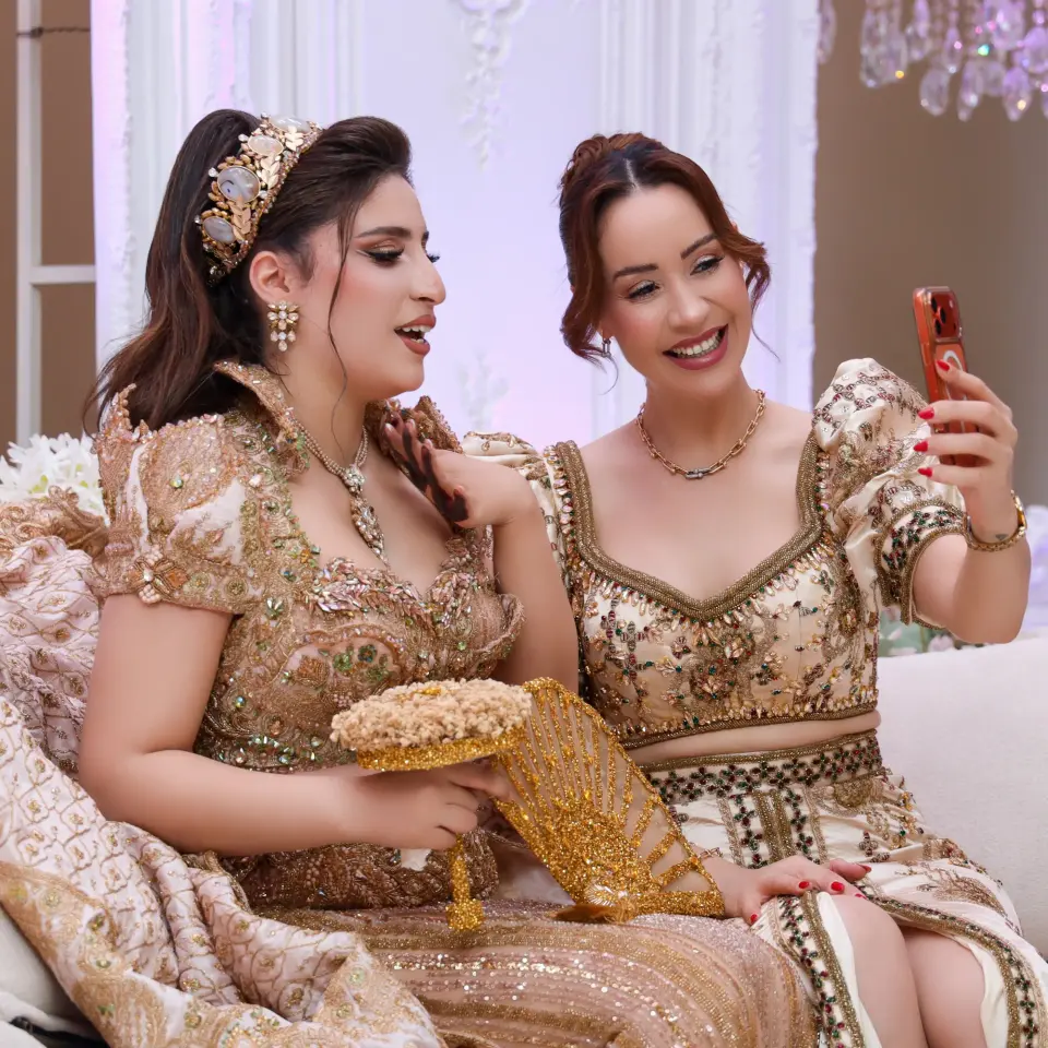 Deux femmes en tenues traditionnelles dorées prenant un selfie pendant la fête