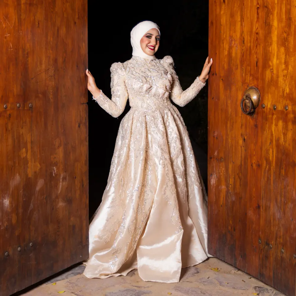 Mariée en robe brodée ivoire entre deux grandes portes en bois ouvertes sur la nuit